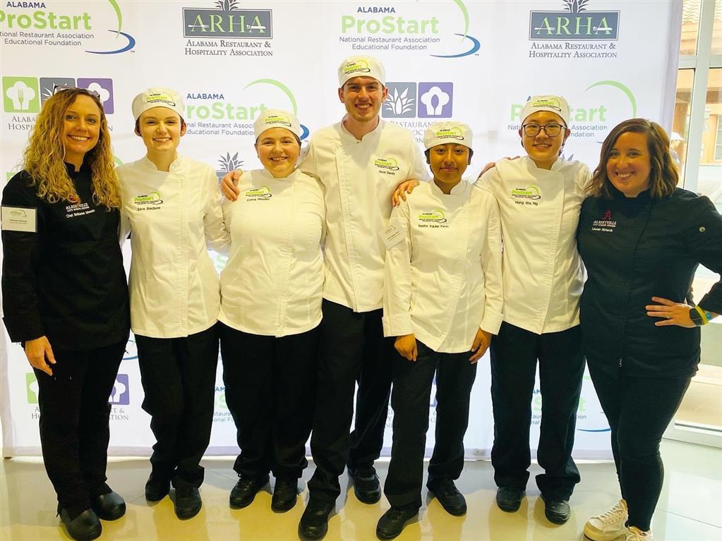 students and teachers standing in chef's aprons and hats.